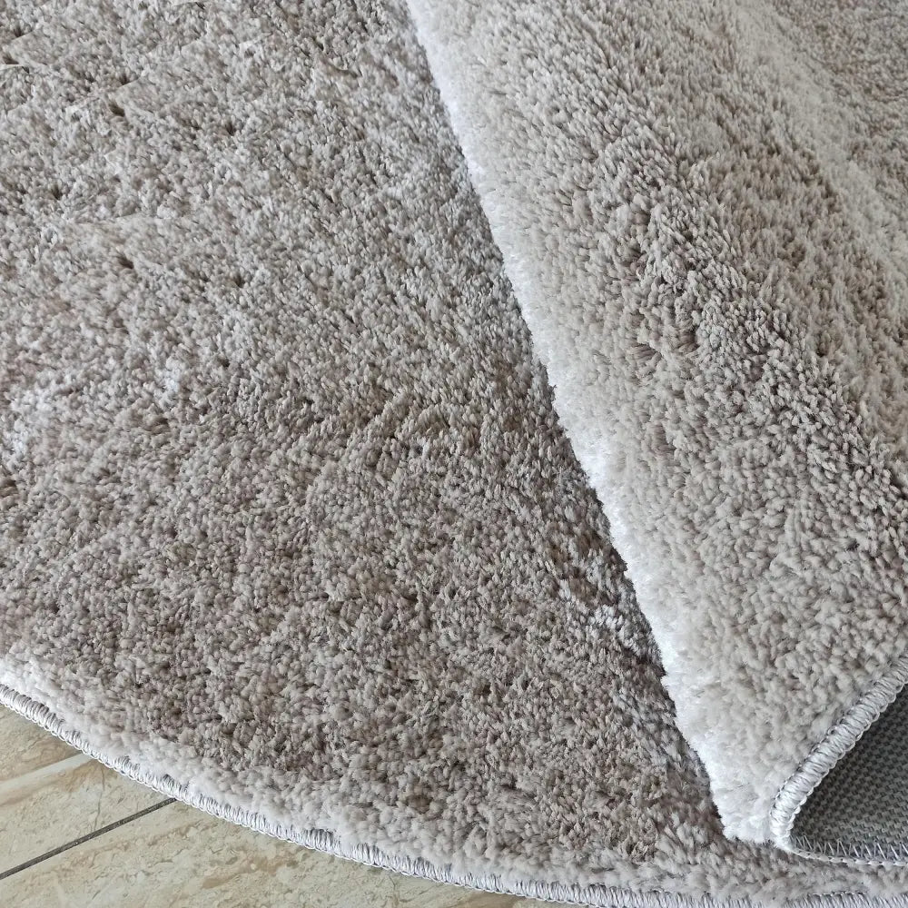 Kamel RundTepe Latte ecru, nærbilde av kort lugg og underside med brettet hjørne på teppet.