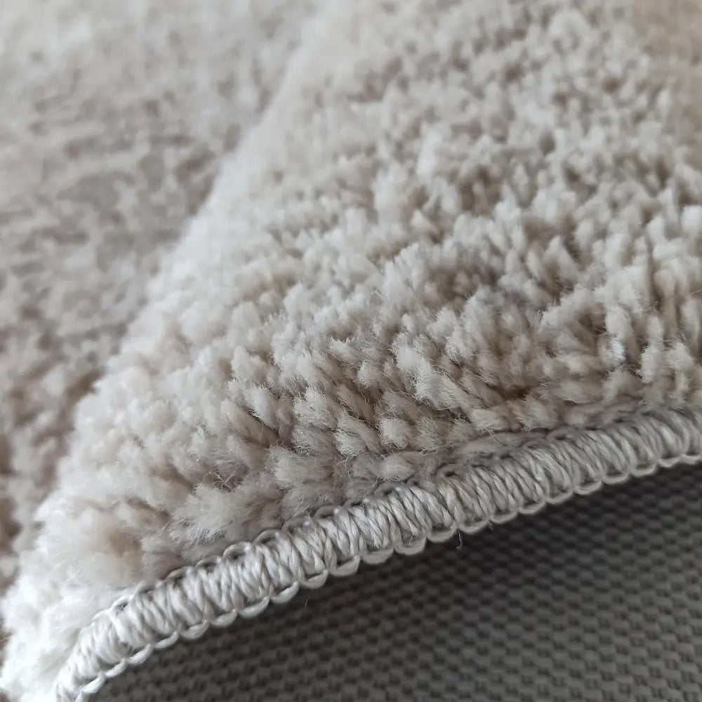 Kamel RundTepe Latte ecru, nærbilde av tykk beige lugg, sømkant og delvis synlig vevd underside.