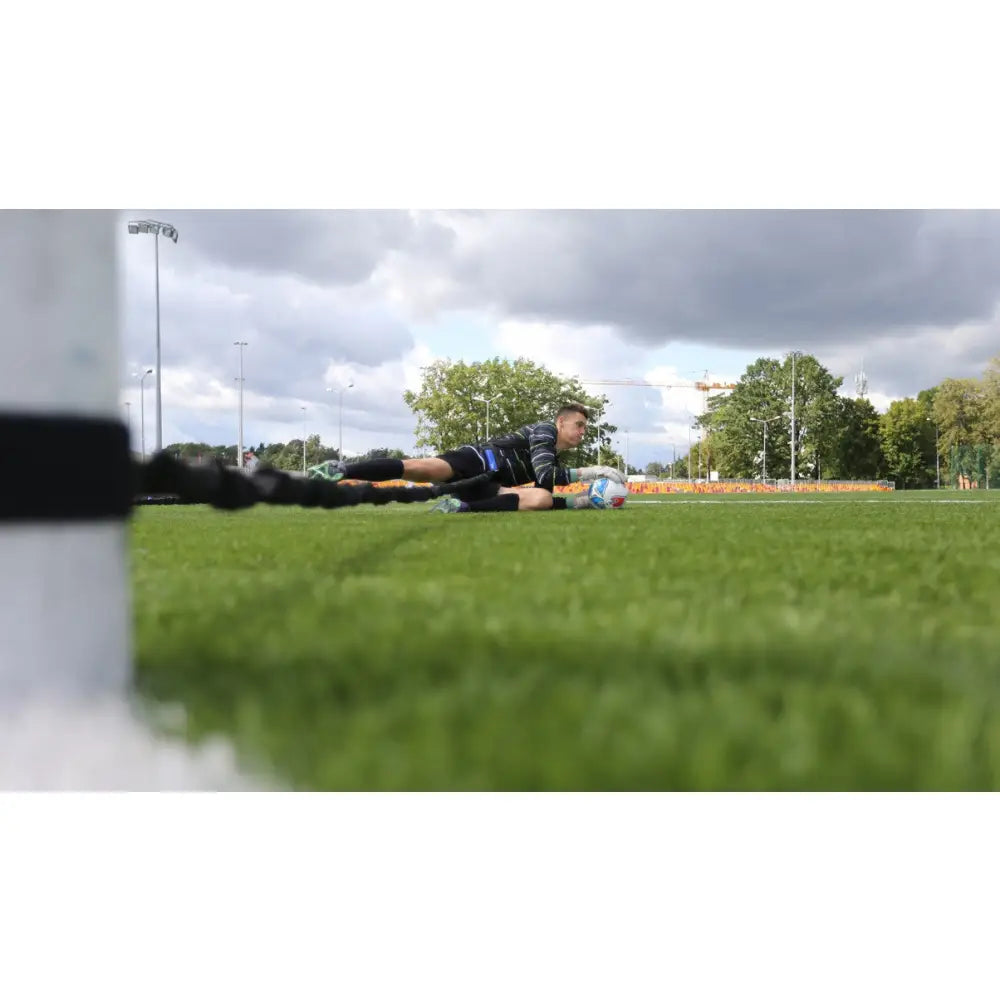 Keeper Treningkummi, lav vinkel av fotballspiller på kunstgress som holder ball og er festet i strikk til stolpe.