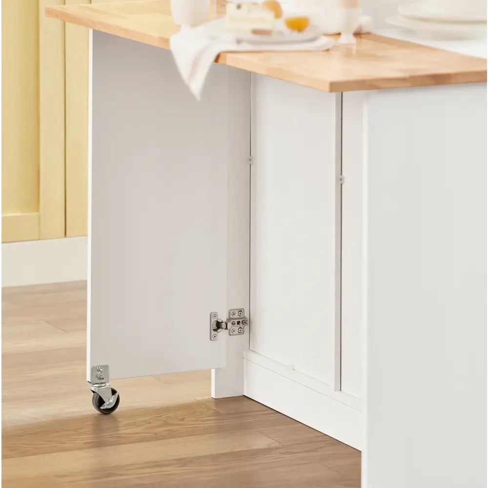Kjøkkenøy med skap og sammenleggbar barstol sett fra siden, hvit bordplate på hjul og treplate med borddekking.