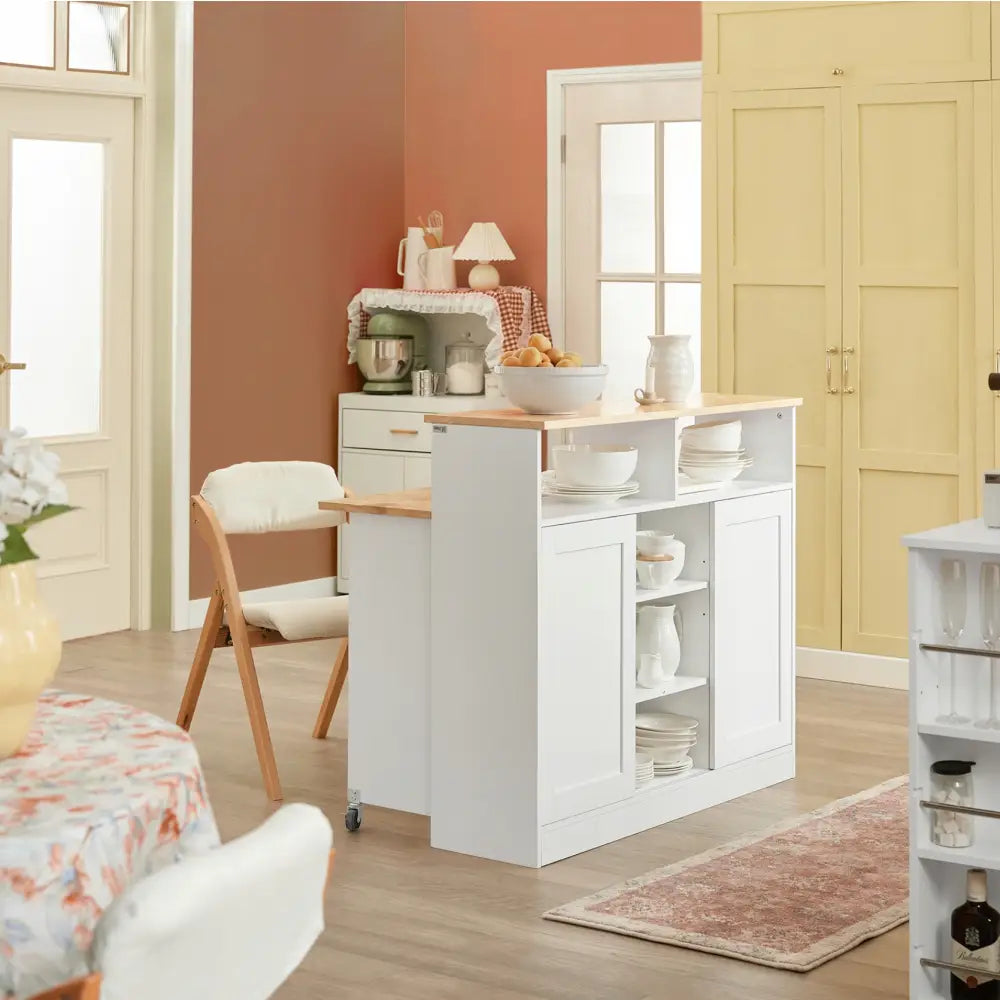 Kjøkkenøy i hvitt med treplate, åpne hyller med servise og stor fruktbolle på toppen, vist fra skrå vinkel.