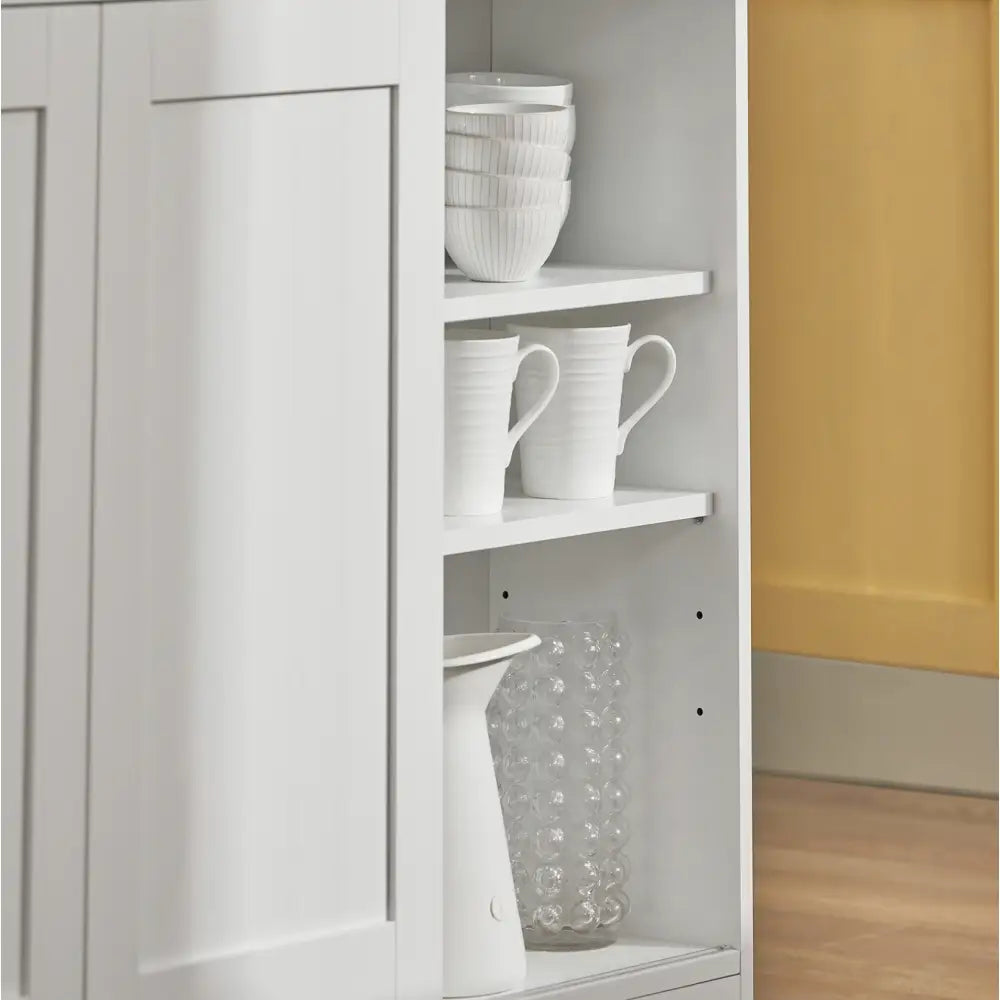 Kjøkkenøy med åpen hylle, stablede hvite skåler og krus, hvit mugge og strukturert glassvase fra siden.