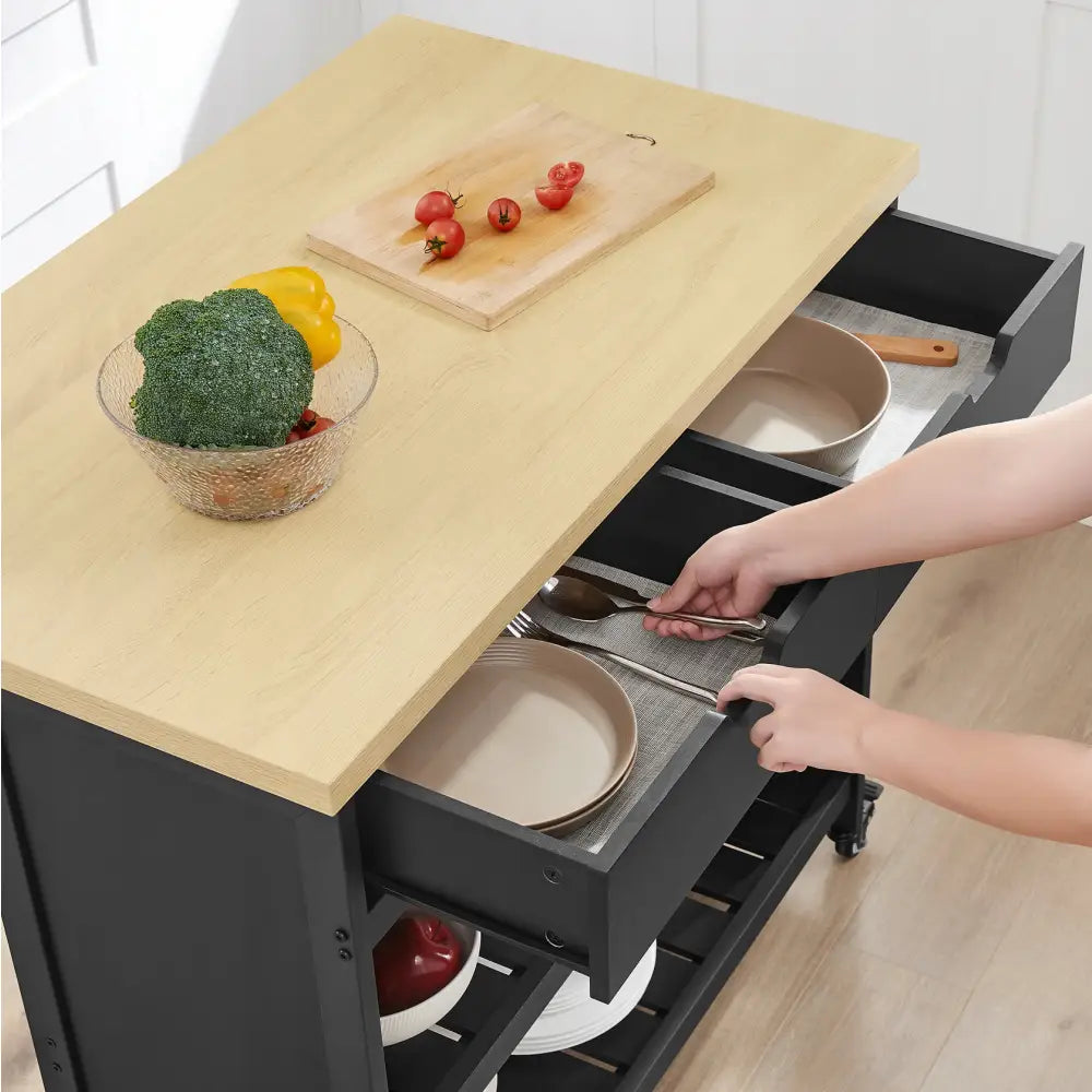 Kjøkkenøy på hjul i eik, sett ovenfra med åpnet skuff fylt med servise og grønnsaker på lys treplate.