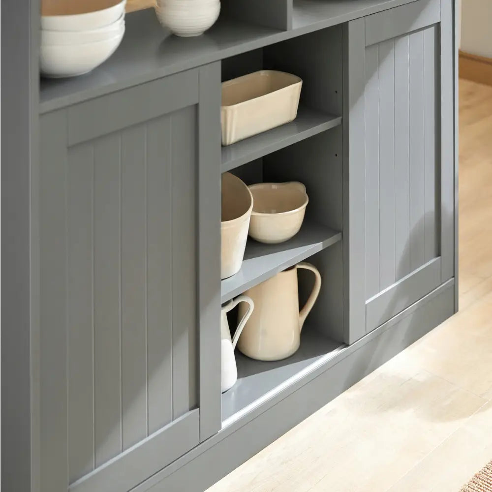 Kjøkkenøy med grå rillede fronter, åpne hyller med keramikkboller og mugger, sett fra siden på lyst gulv.