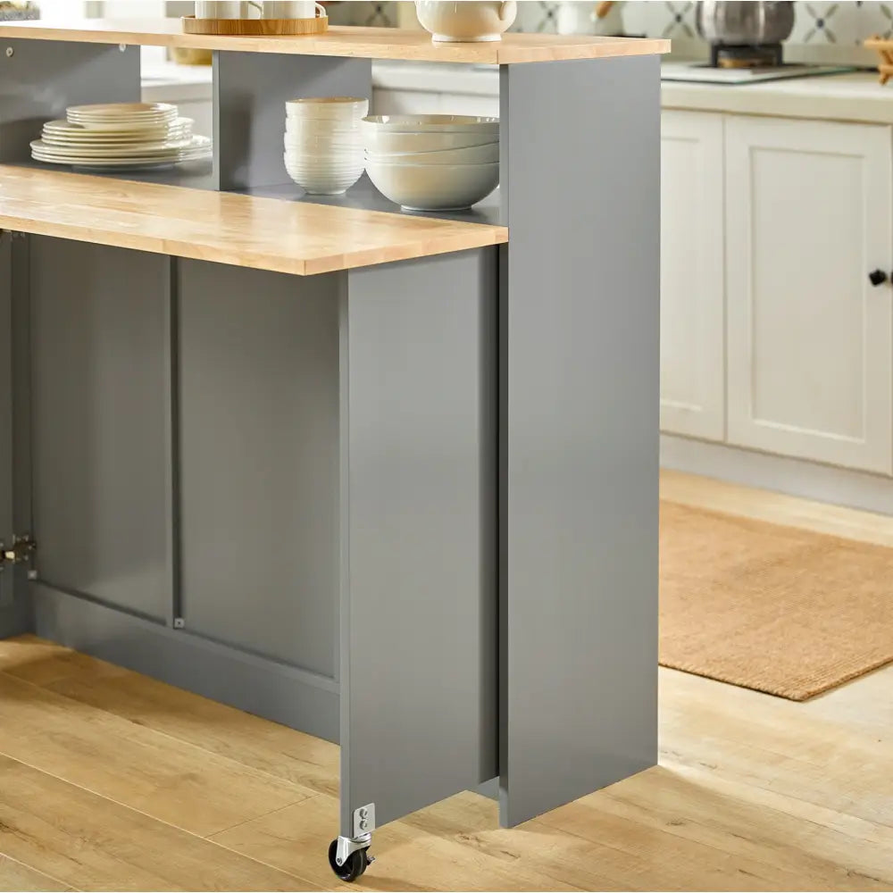 Kjøkkenøy med sammenleggbar bartable, grå finish, arbeidsplate i lyst tre og åpne hyller med servise.