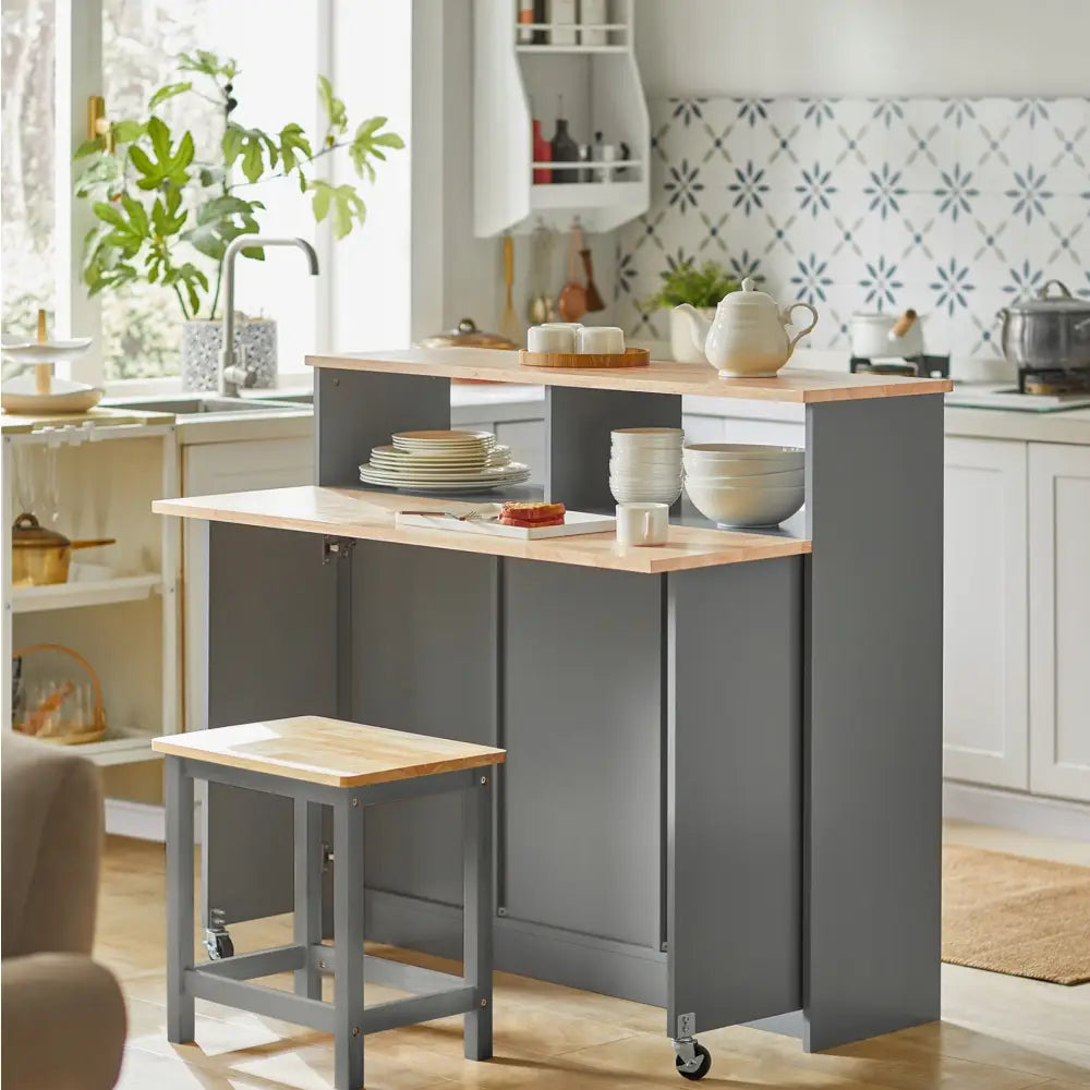 Kjøkkenøy skap med sammenleggbar bartable, grå med lyse treplater, krakk og åpne hyller med servise.