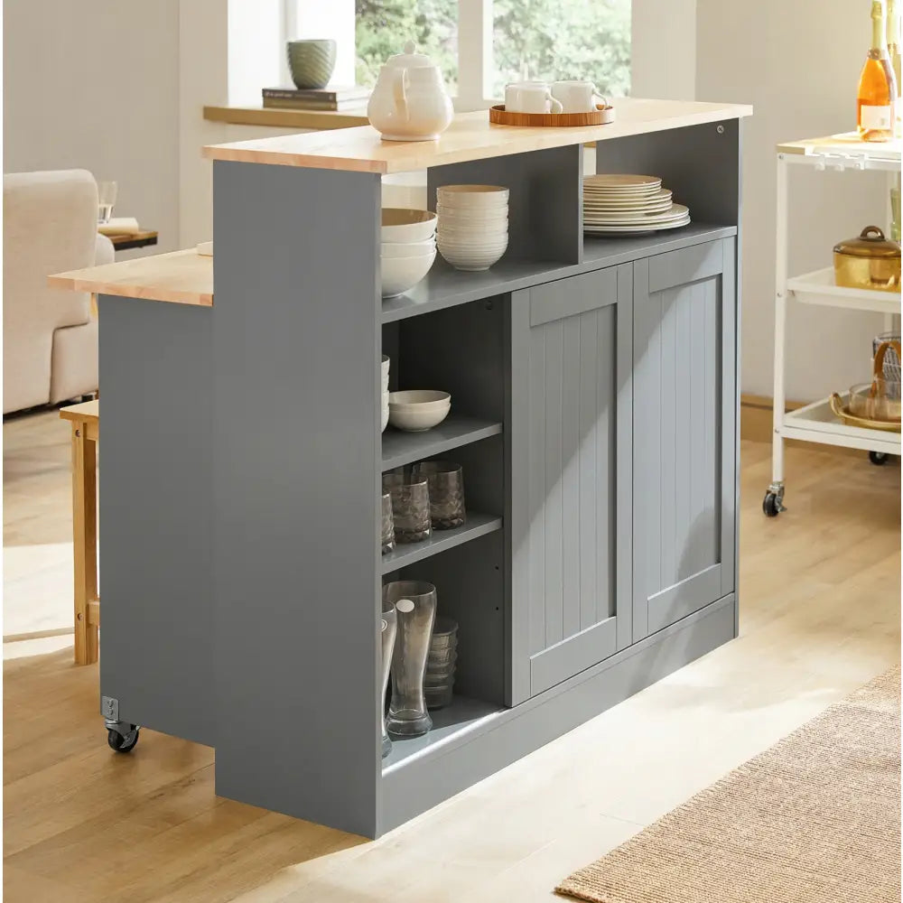 Kjøkkenøy med grå ramme, lyse treflater, åpne hyller fylt med servise og glass, sett fra siden.