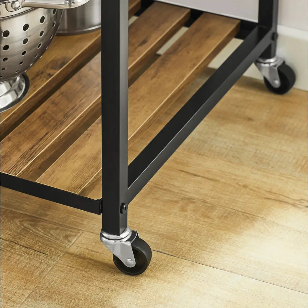Kjøkkentrolley med svarte metallben og hjul, nærbilde av lys trehylle og robust hjørnekonstruksjon.