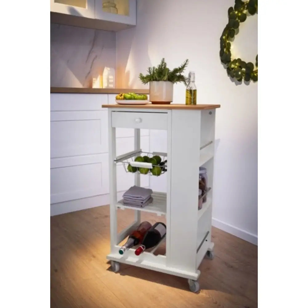 Kjøkkenvogn med hvit ramme og treplate, skuff, epler i kurv, hyller med vinflasker og kjøkkenhåndklær.