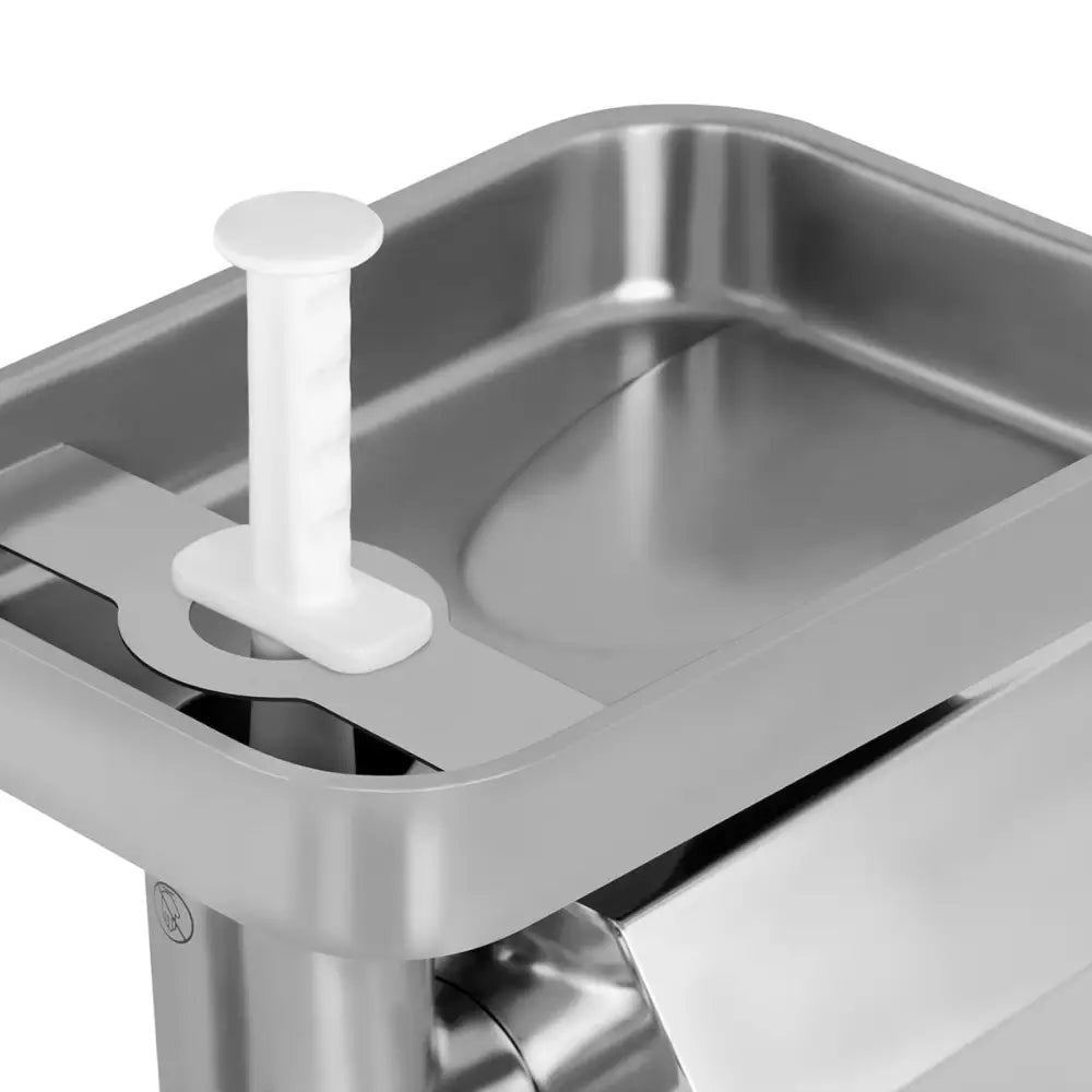 Kjøttkvern i rustfritt stål, nærbilde av metalltrau med avrundede hjørner og hvit plaststapper stående oppreist.