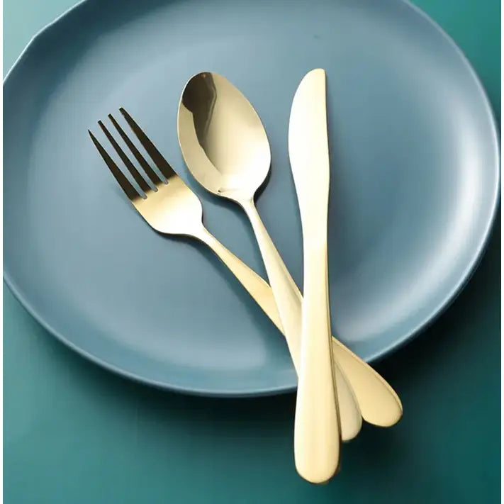 Gullfarget bestikksett med blank finish, elegant plassert på matt blå tallerken, sett ovenfra.