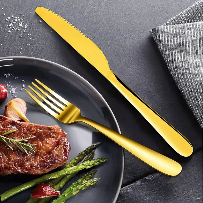 Klassisk bestikksett i gull, kniv og gaffel ved siden av mørk tallerken og stripete serviett på mørkt bord.