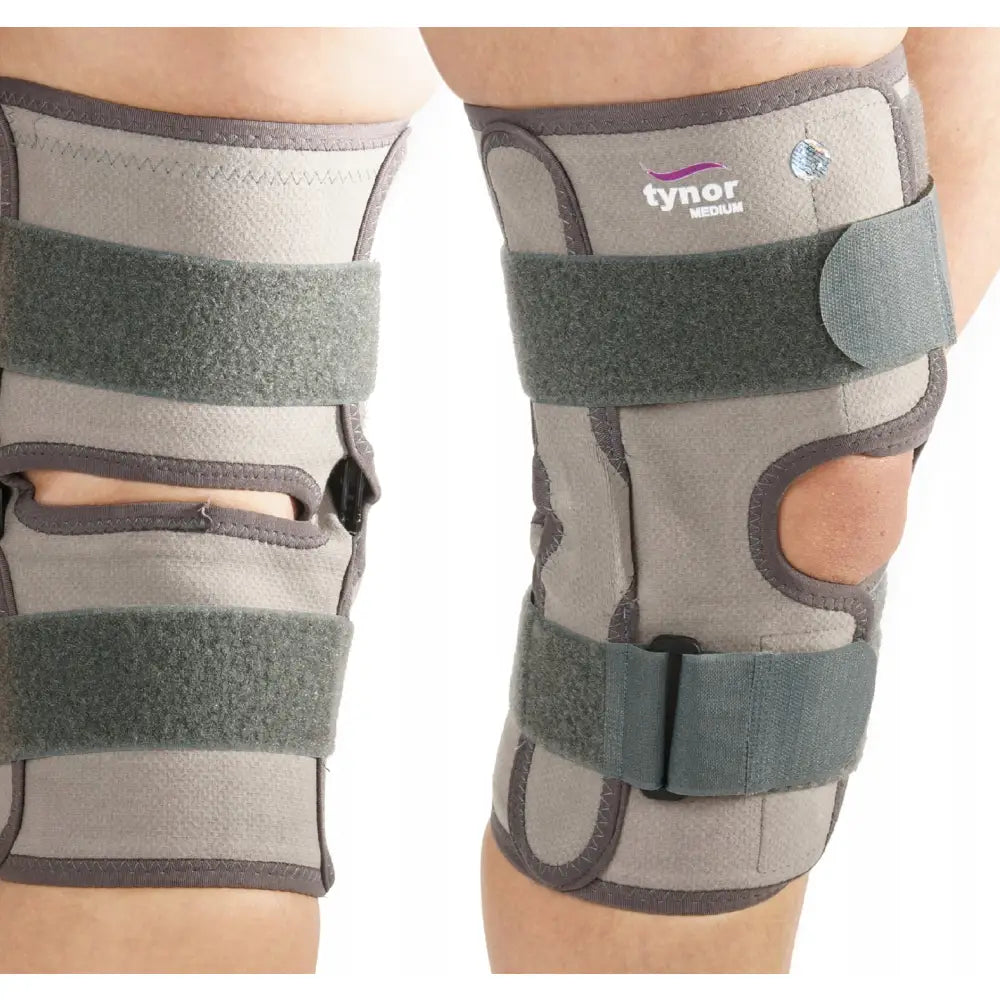 Knestabilisator med skinner, grå ortose på ben med brede borrelåsbånd og åpninger rundt kneleddet.