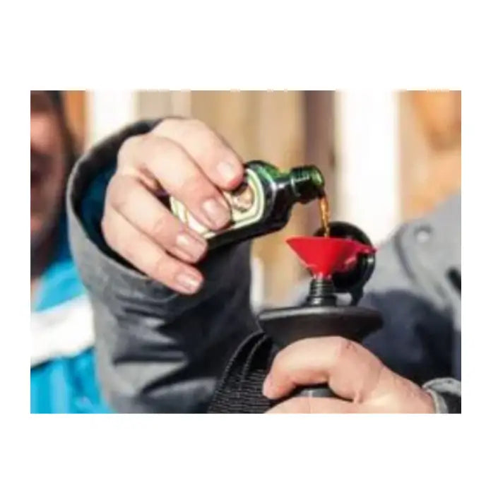 Komperdell Schnapsstock skistav brukt til å helle væske fra grønn flaske via rød trakt i svart beholder, nærbilde.