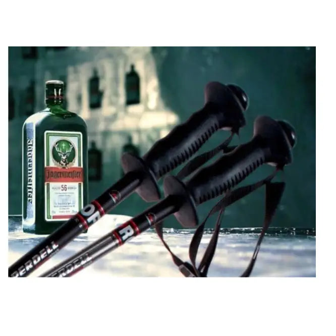 Komperdell Schnapsstock skistaver, svarte med ergonomiske håndtak, håndstrikker og grønn flaske ved siden av.