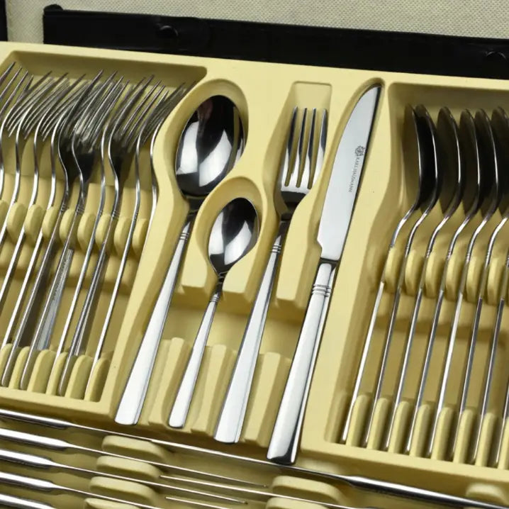 Komplett bestikksett i blankt rustfritt stål, organisert i beige brett, sett ovenfra med fokus på bestikkdeler.