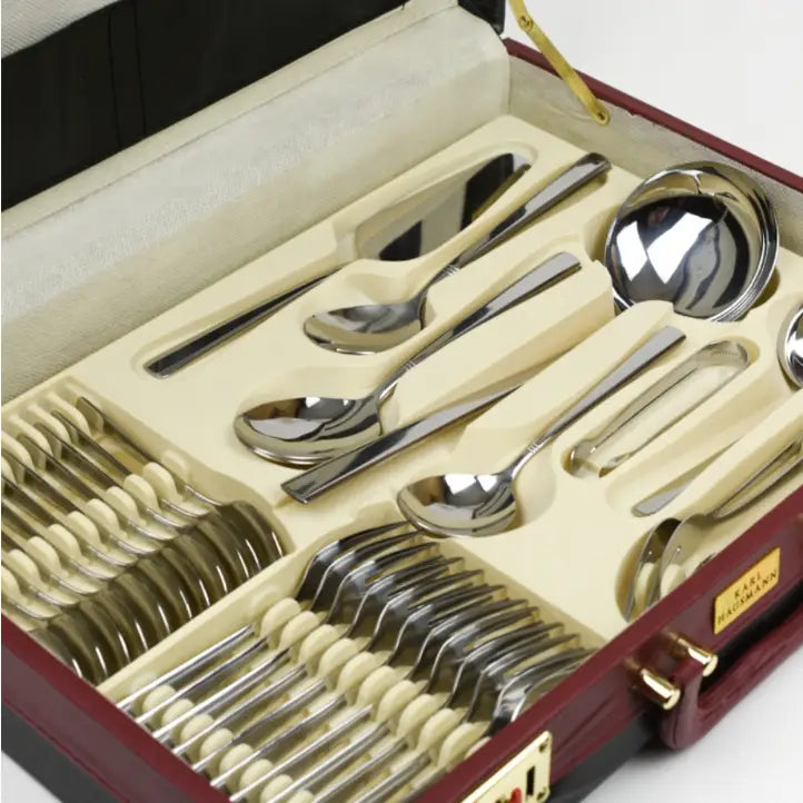 Komplett bestikksett med 72 blanke deler, pent arrangert i beige innsats i rød koffert, sett skrått ovenfra.