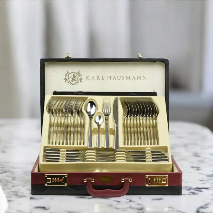 Komplett bestikksett i sølvfarge, elegant arrangert i åpen rød og sort koffert med gullåser på marmorbord.