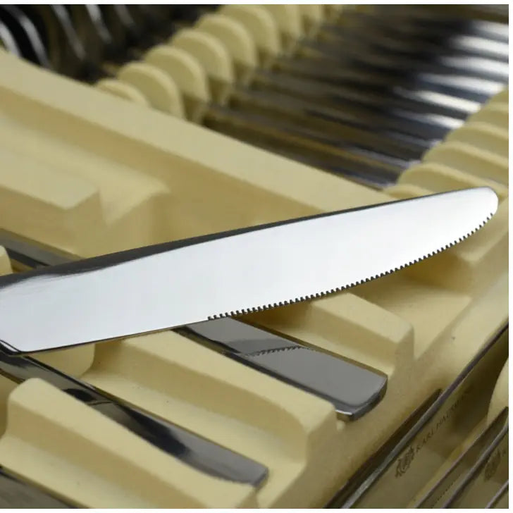 Blankt riflet knivblad i rustfritt stål, skrått plassert i beige bestikkinnlegg sammen med annet bestikk.