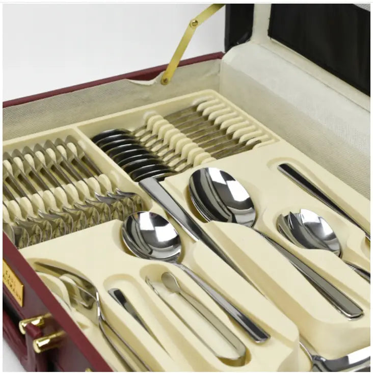 Komplett bestikksett i rustfritt stål, elegant oppstilt i kremfarget innsats i åpen koffert, skrå oversiktsvinkel.