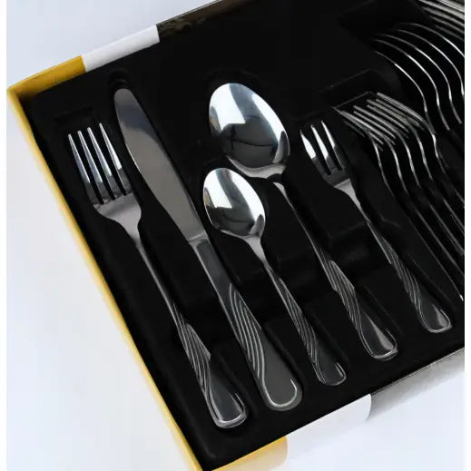 Bestikksett i blankt rustfritt stål, sett ovenfra i eske, med bølgede håndtak på gafler, kniver og skjeer.