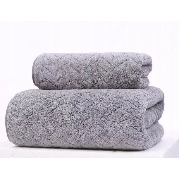 Komplett håndklesett i grå mikrofiber, to myke håndklær med fiskebensmønster brettet og stablet fra siden.