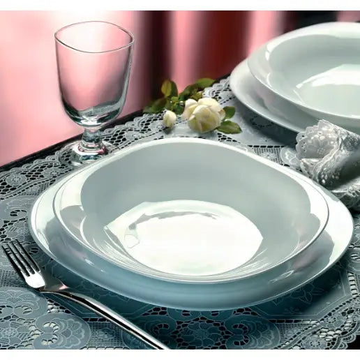 Parma dyp porselenstallerken sett ovenfra på bord med blondeduk, glass, bestikk og blomsterdekor.