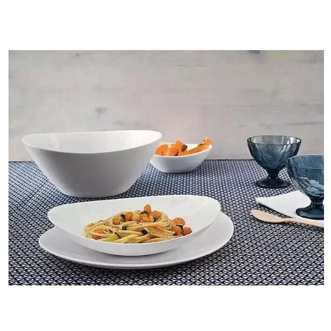 Komplett servise sett med hvite ovale porselenstallerkener, servert pastarett på blåmønstret duk med blå glass bak.