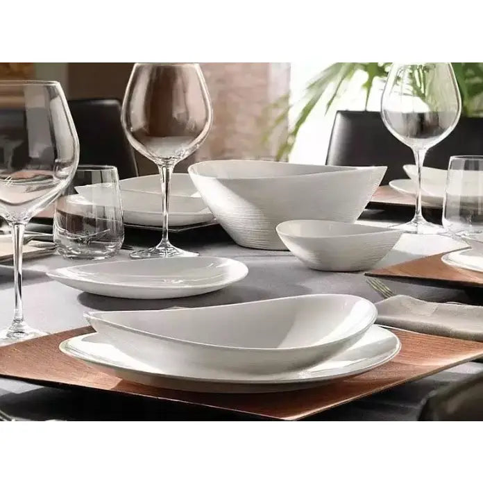 Komplett servisesett med hvite, organiske tallerkener og skåler, dekket til seks med vinglass og moderne borddekor.