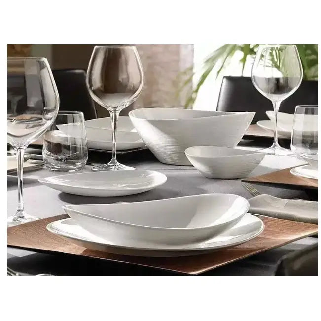 Komplett servise sett i hvitt porselen, middagstallerkener og boller arrangert på mørk duk med glass.