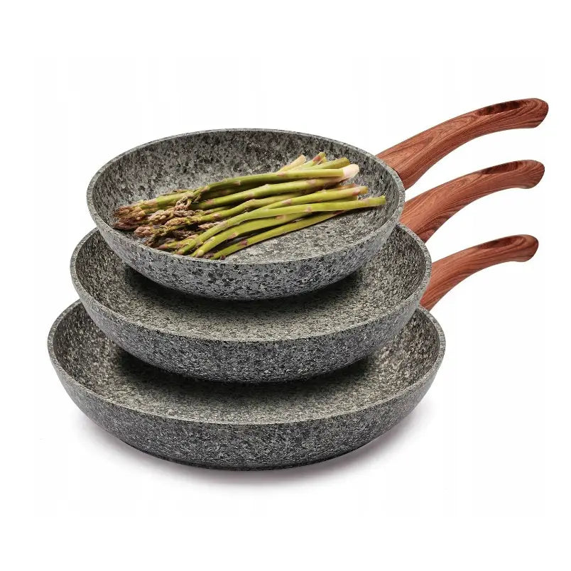 Komplett sett med Konighoffer stekepanner i grå stein-look, stablet med grønne asparges i øverste panne.