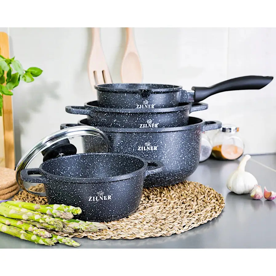 Komplett sett med marmorbelagte gryter i ulike størrelser, stablet med glasslokk, asparges foran på benken.