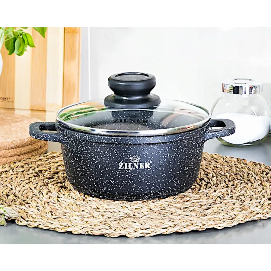 Sort gryte med hvite prikker og glasslokk, sidevisning på flettet bordbrikke, del av marmorbelagt sett.