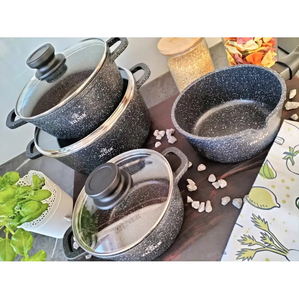 Komplett sett med sorte marmorbelagte gryter og kasseroller med glasslokk, skrå oversiktsvisning på kjøkkenbenk.