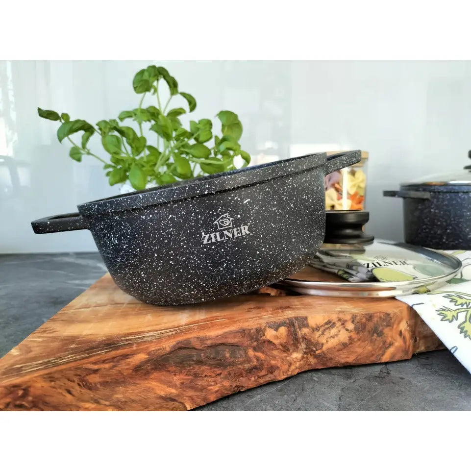 Sort gryte med marmorbelegg og hvite prikker, lokk ved siden av, plassert på skjærebrett i tre.