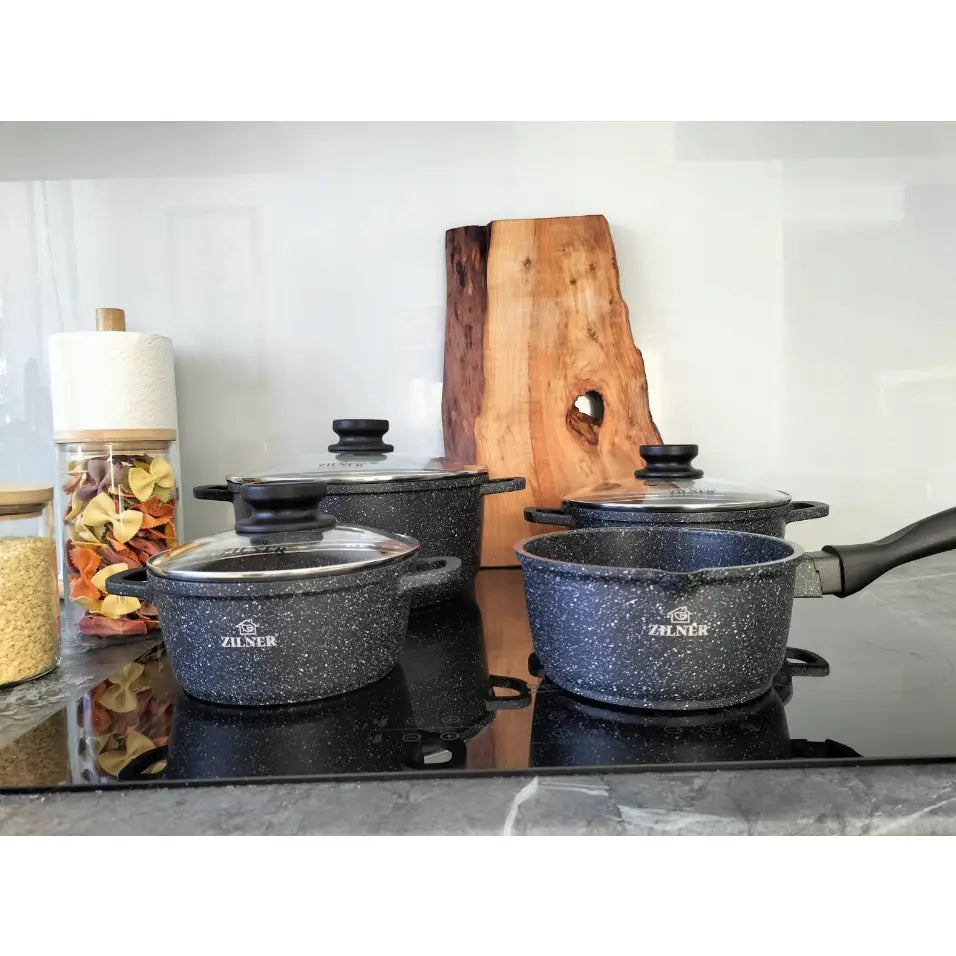 Komplett marmorbelagt grytesett, fire sorte gryter med hvite prikker og glasslokk på induksjonsplate.