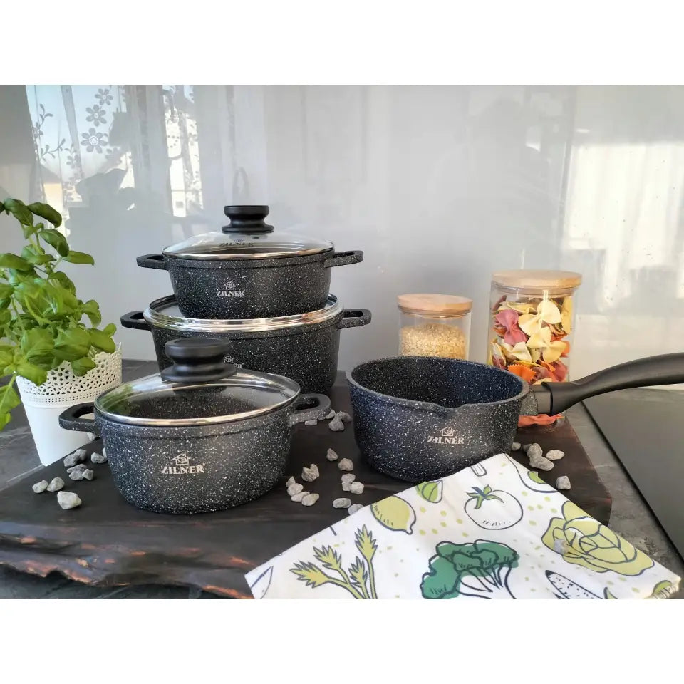 Komplett sett med mørkegrå marmorbelagte gryter og kasseroller med glasslokk, plassert på kjøkkenbenk med urter.