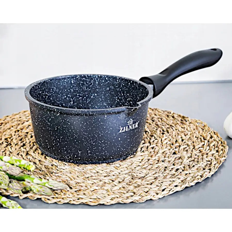 Sort marmorbelagt gryte med ergonomisk håndtak, sett fra siden på flettet brikke, asparges foran.