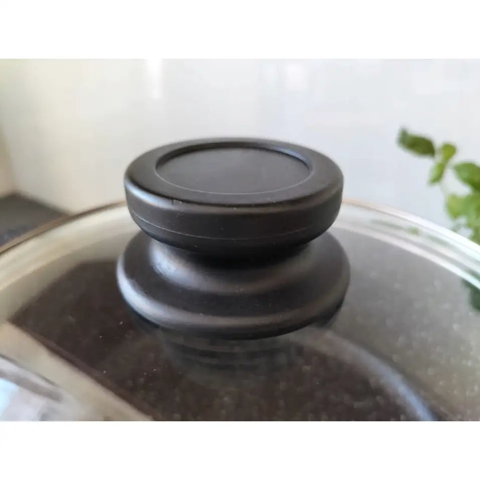 Sort plasthåndtak på glasslokk til marmorbelagt gryte, nærbilde som fremhever matt finish og enkel design.