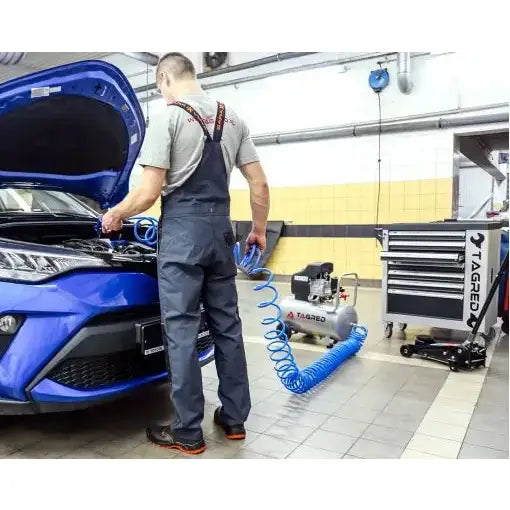 Kompressor 24L 8 bar i bruk på blå bil, mann i arbeid med spiralslange i verkstedmiljø, sidevisning.