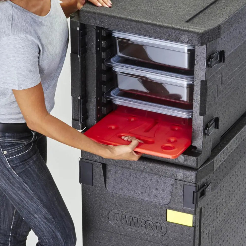 Kontainer termobox EPP CAMBRO med åpen dør, tre GN-bakker og rødt kjøleelement settes inn av en person.