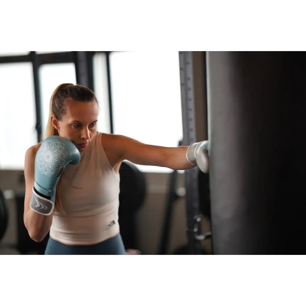 Kvinners boksehanske Mandala i blått og grått, brukt under slag mot svart boksebag på treningssenter.