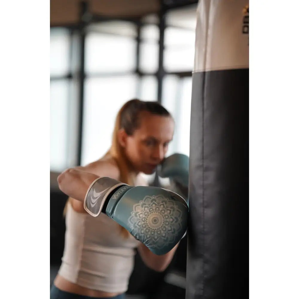 Lyseblå boksehanske med mandalamønster bæres av kvinne som bokser mot svart boksepute.