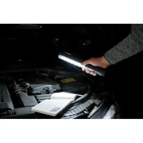 LED arbeidslykt med batteri og dynamo, lyser opp bilmotor i mørket mens et hefte ligger åpent på motoren.