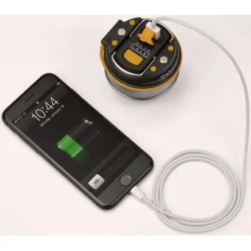 Lampe LED OLI, sort og gul, vist ovenfra mens den lader en mobil via hvit USB-kabel, kontrollknapper synlige.