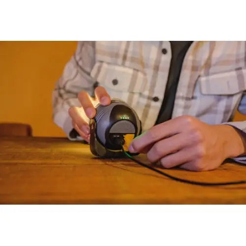 Lampe LED OLI 310 AB med høyttaler, nærbilde av enhet koblet til strøm på trebord, holdt av person.