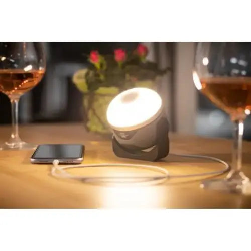 LED-lampe OLI 310 AB med Bluetooth-høyttaler, lyser opp bord med vinglass, mobil og blomster.