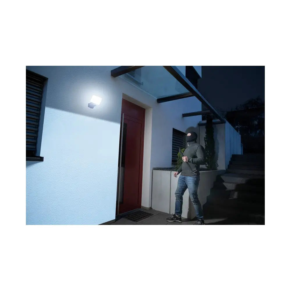 Utendørs WiFi-lampe lyser opp inngangsparti om natten, person med ansiktsmaske nær døren.