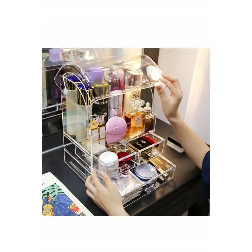 Låsbar sminkeorganisator i klar plast med åpnet buet lokk, viser rom og skuffer fylt med sminke.