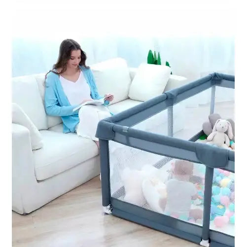 Lekegrind for barn med skummatte, sett fra siden, barn leker blant baller og kosedyr ved siden av sofa.